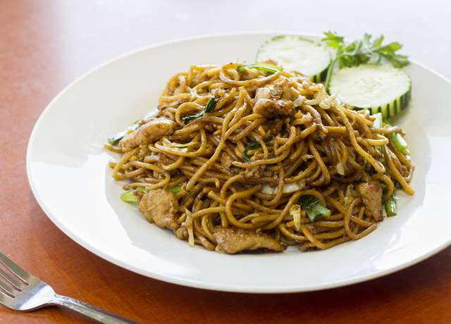 Semangkuk mie tek-tek lengkap dengan sayuran segar, bakso, dan telur, disajikan panas dengan taburan bawang goreng dan seledri